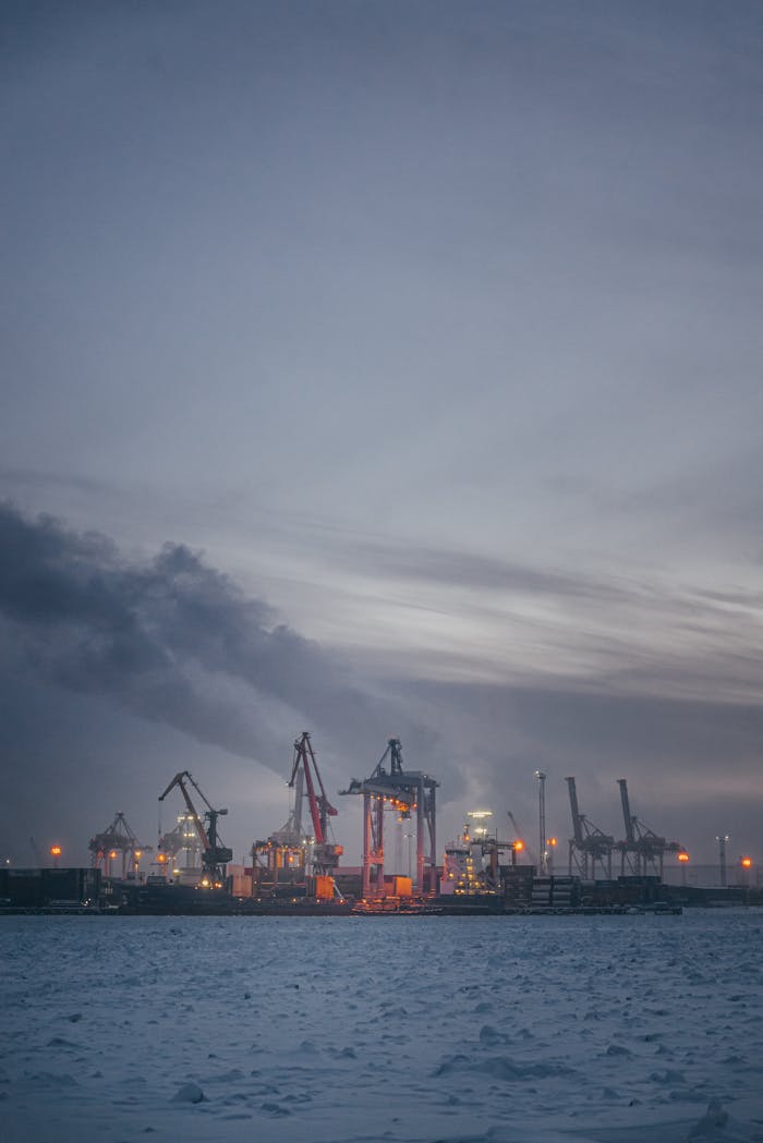 A serene view of an industrial sea port at twilight with cranes and smoke.